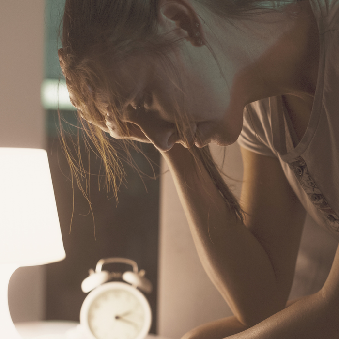 woman with head in her hands, tired. In a dimly lit bedroom with a night light on and an alarm clock