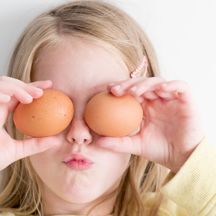 Young girl holding two eggs up in front of her face in a playful gesture