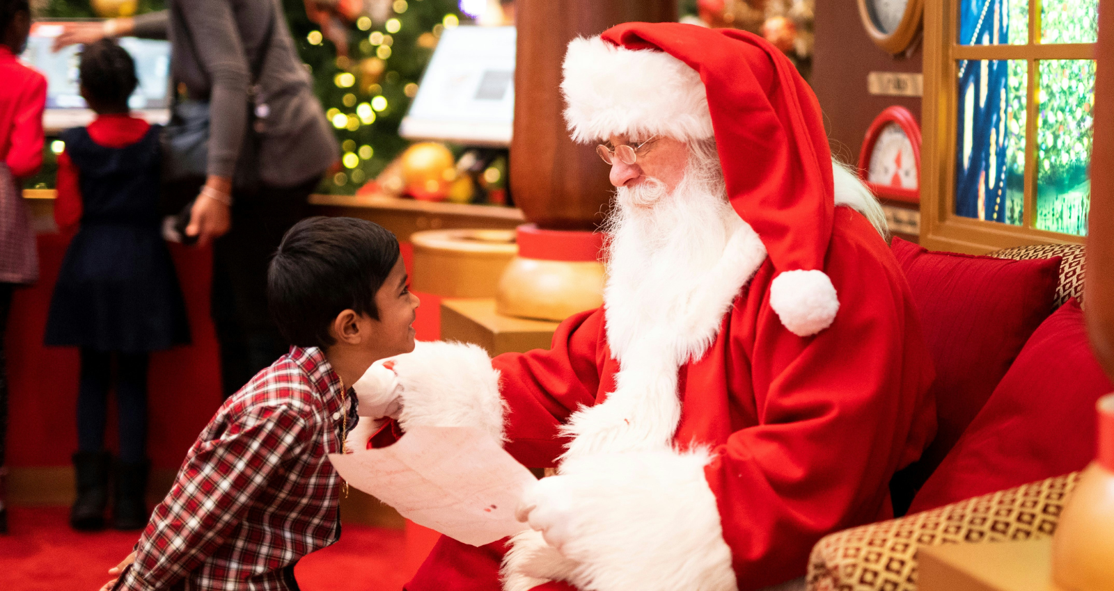 Child leaning towards a man dressed as santa in a cosy setting